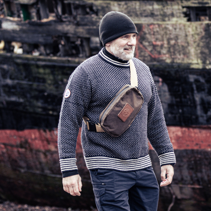 Man walking past shipwreck wearing Gunnerside Sweater and Close Hold Bag