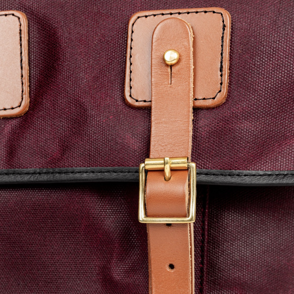 Buckle strap detail of a Gubbins messenger bag in burgundy color